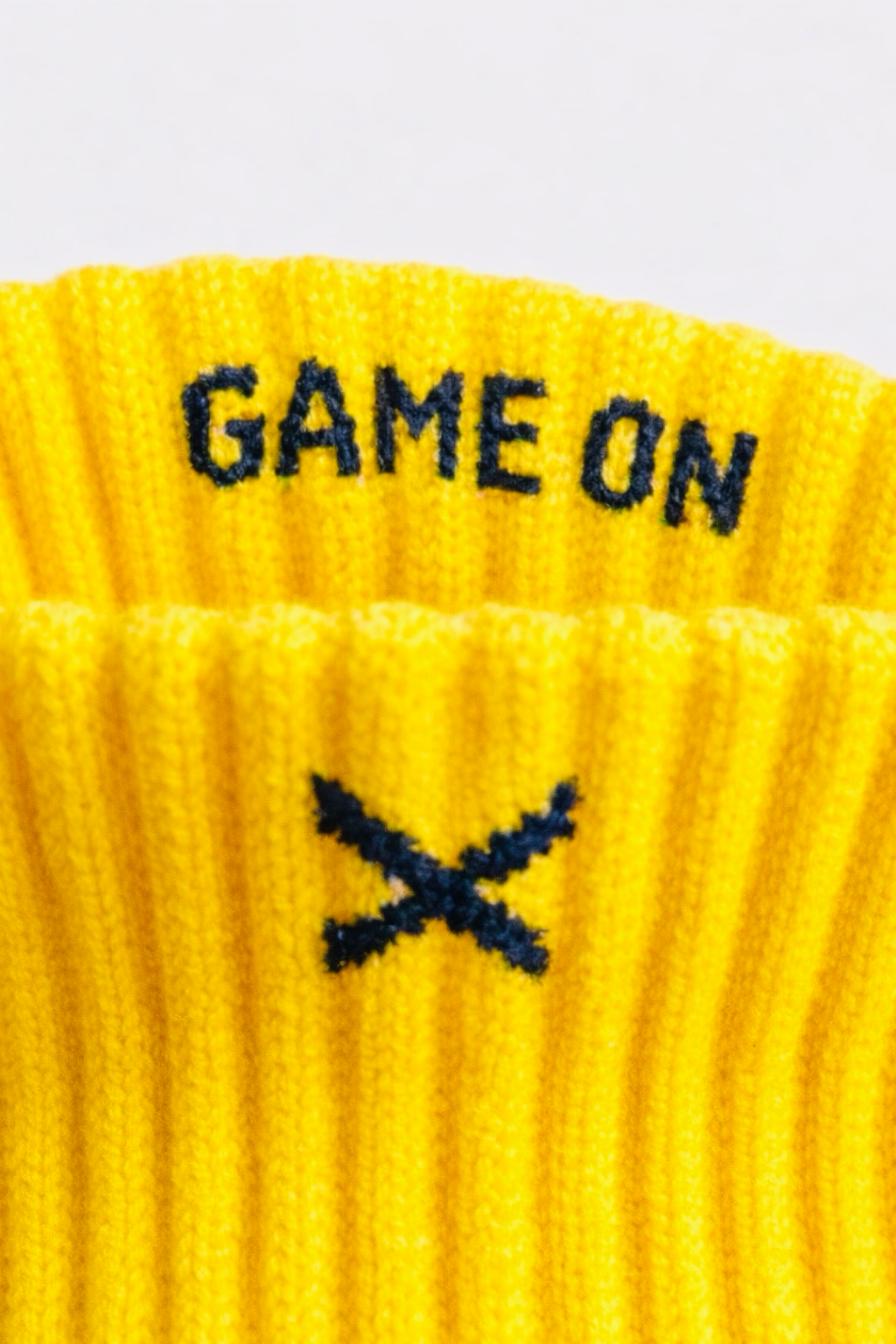 Detalj av gul EliteX™ Gripsokker – Gul med teksten "GAME ON" og et svart kryss i strikket materiale, designet for optimal grep og komfort.